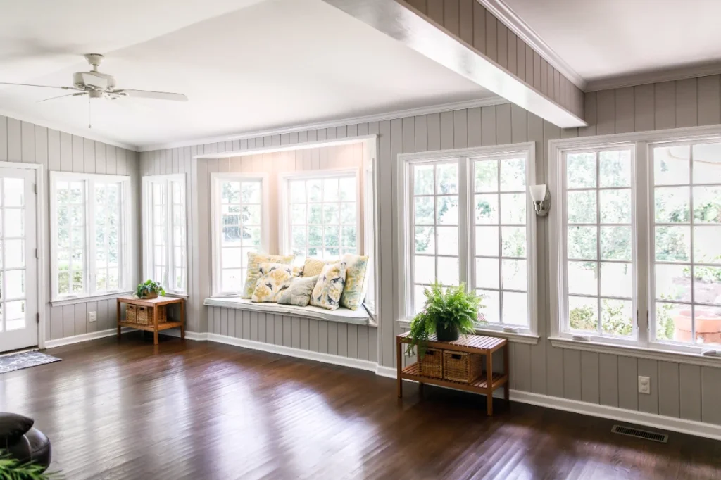 Bright sunroom with window seat, gray shiplap walls, and hardwood floors