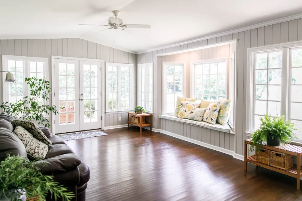 Bright sunroom with gray shiplap walls, window seat, hardwood floors, and French doors