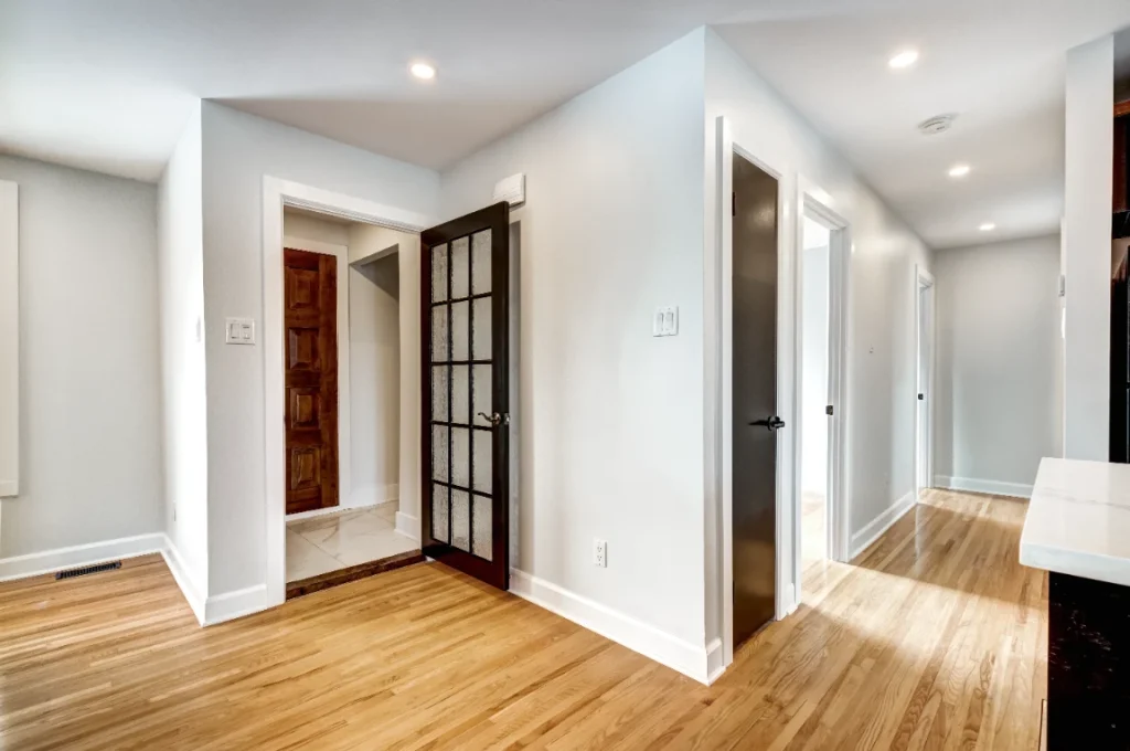 Bright empty hallway with hardwood floors, white walls, and mixed interior doors