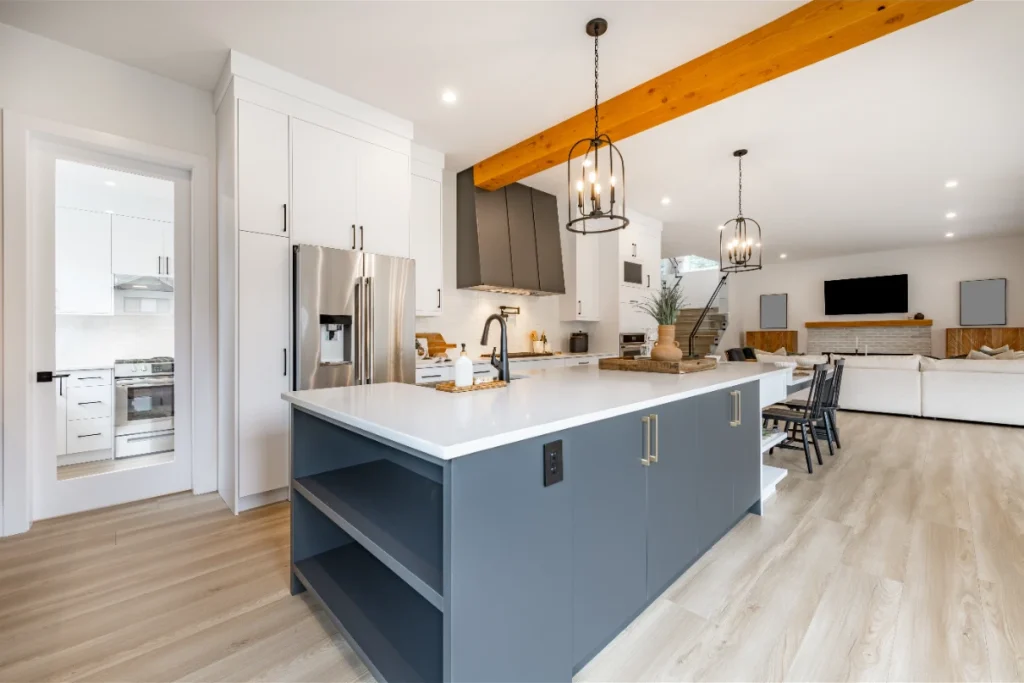 Modern open-concept kitchen with blue island, white cabinets, exposed wood beam, and pendant lights