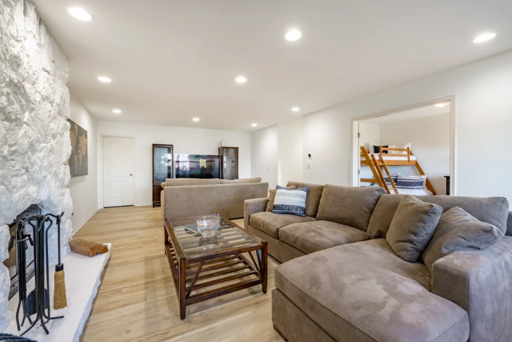 Spacious living room with sectional sofa, stone fireplace, TV, and bunk bedroom visible