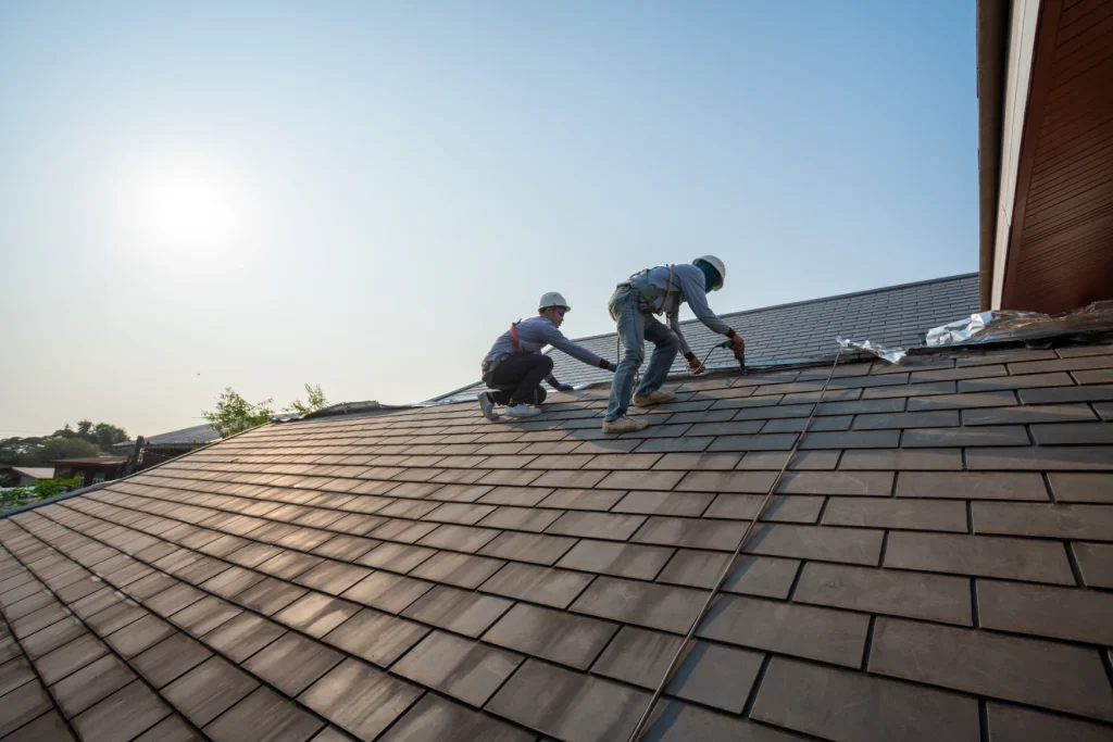 Two roofers in hard hats installing shingles on a residential roof