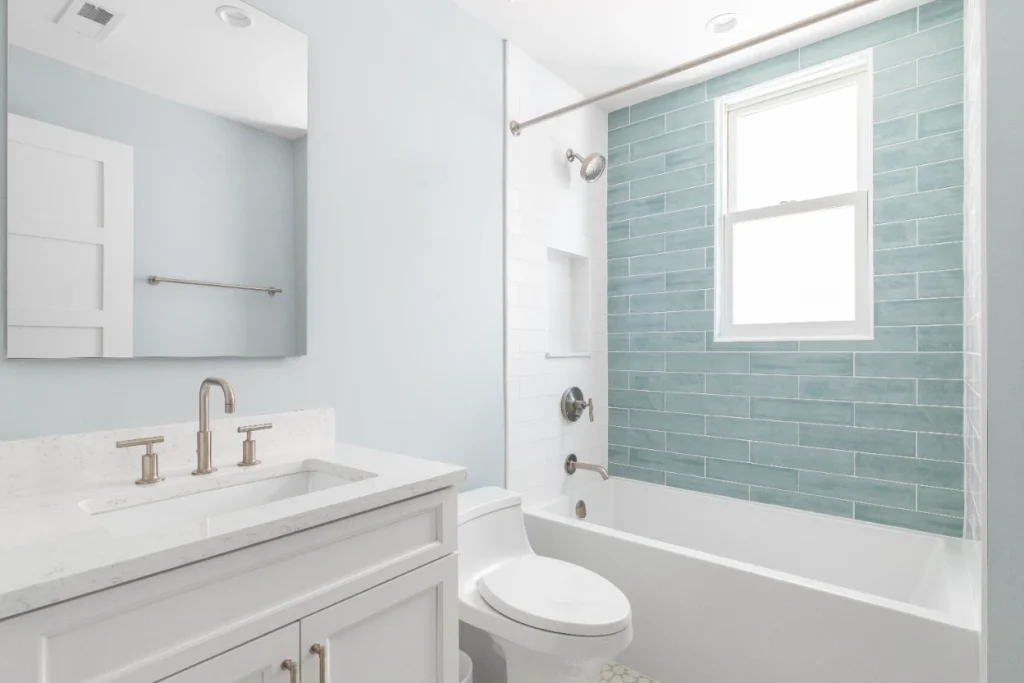 Remodeled bathroom with teal subway tile shower, white vanity, and marble countertop