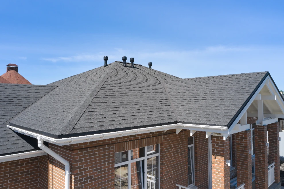Brick house with dark gray asphalt shingle roof and white gutters under blue sky
