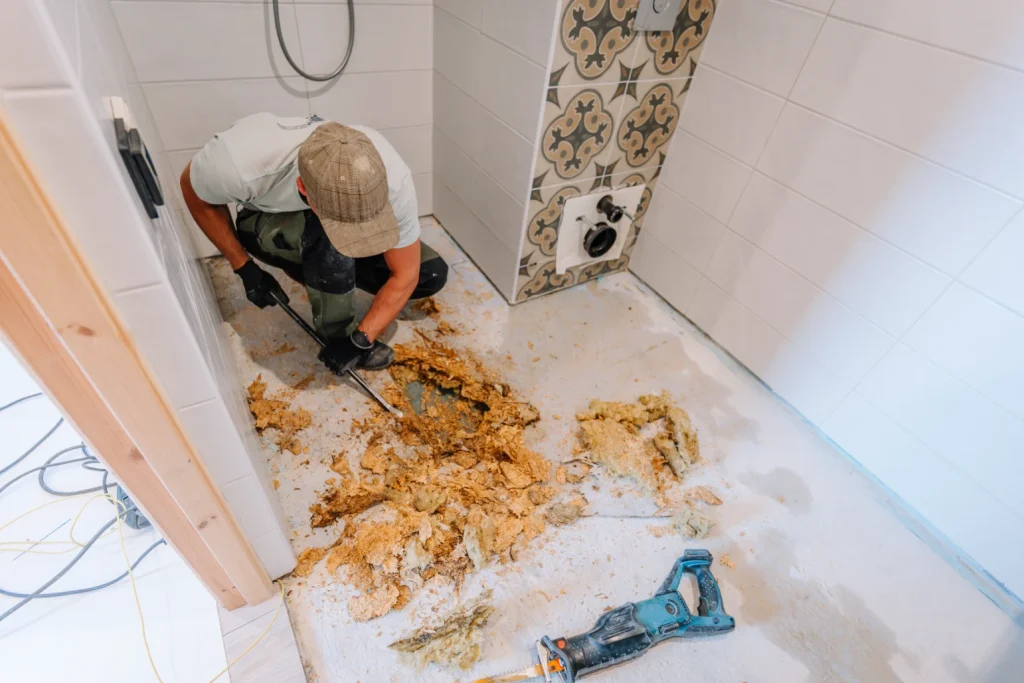 Worker removing old bathroom floor tiles with a chisel during renovation