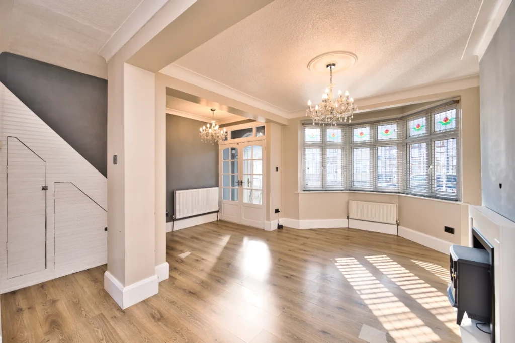 Empty living room with bay window, stained glass panels, chandelier, and wood floors