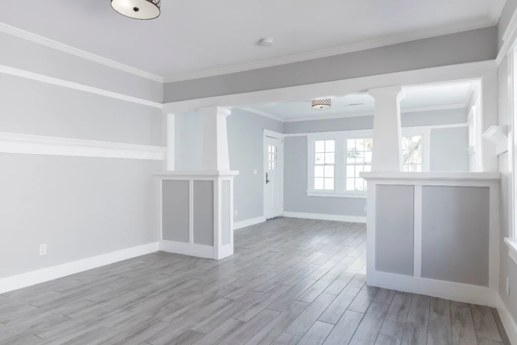 Empty open-plan living space with gray walls, hardwood floors, and white trim columns